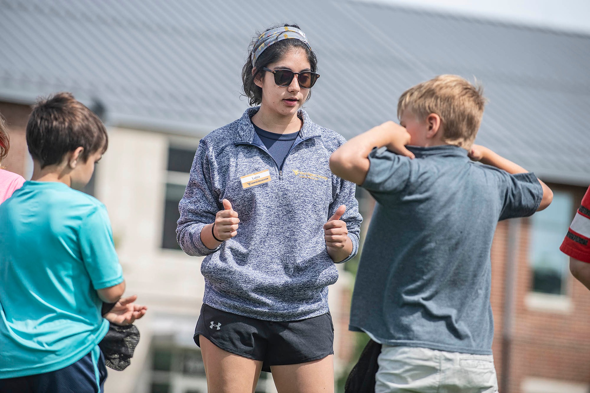 College student gives thumbs up while speaking with two children