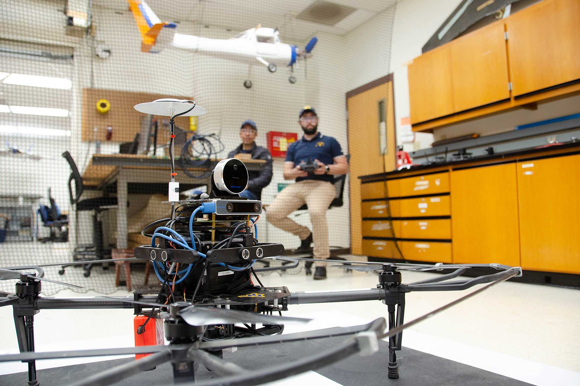 Up-close look at an aerial robot, with a student in the background holding a controller