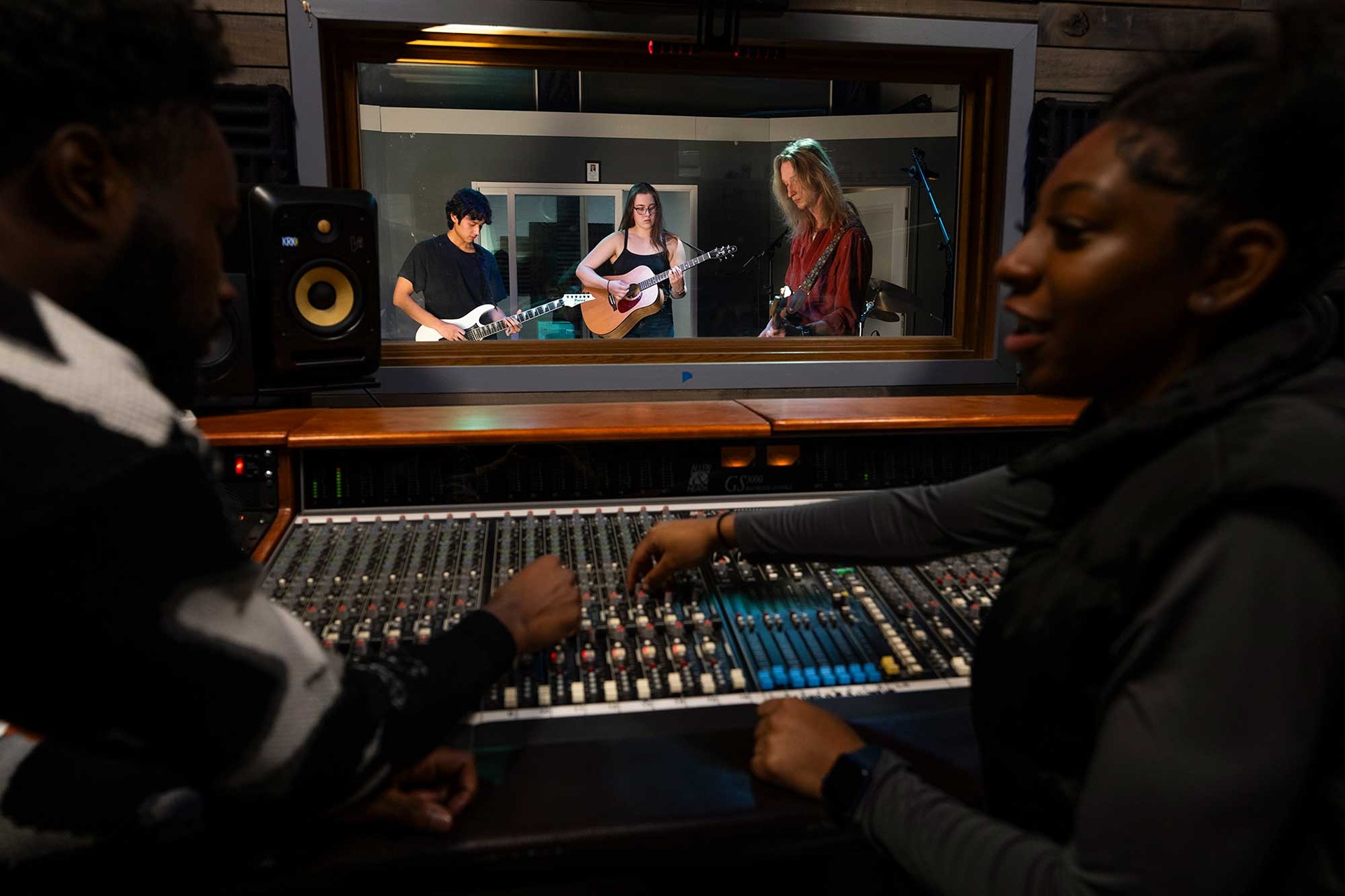 Music Business and Industry student production engineers discuss changes at the board while classmates perform