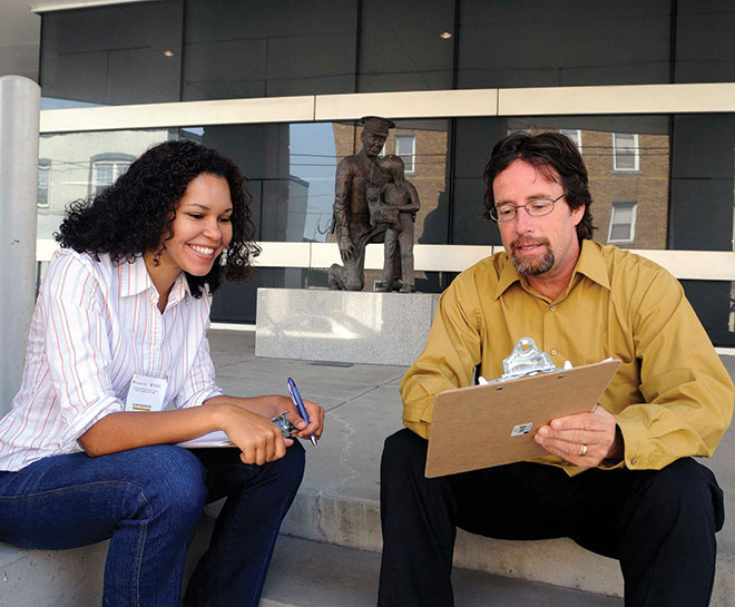 Professor and research assistant discuss research data while seated in front of Morgantown's Public Safety Building.