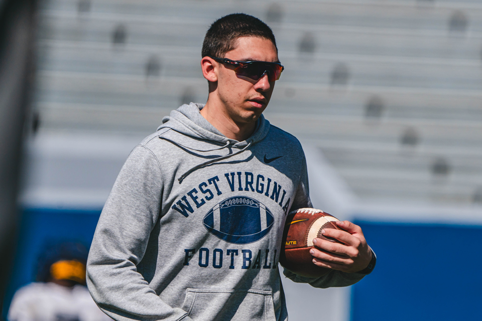 Person wearing a WV Football sweatshirt carries a football.