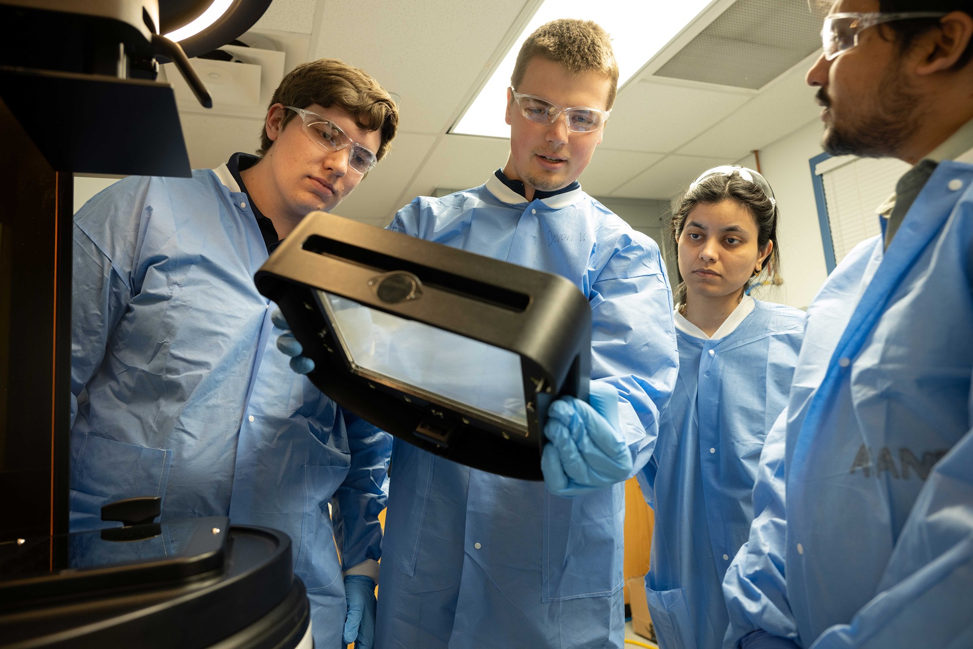 People in protective gear inspect a piece of lab equipment