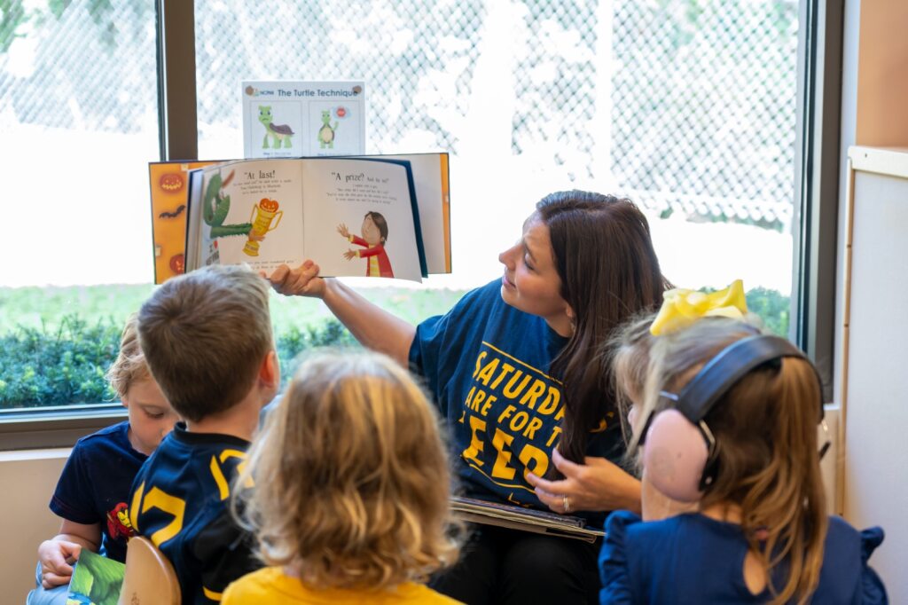 Person holding up a book while reading aloud to a group of children