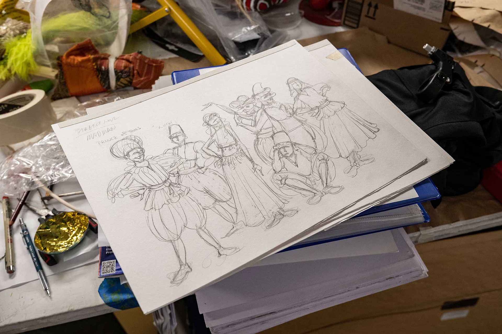 Costume sketches stacked on a work table
