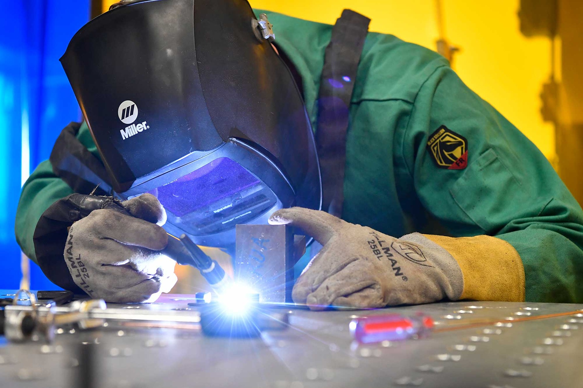 Student wearing a welding helmet and gloves works with metal in the Lane Innovation Hub