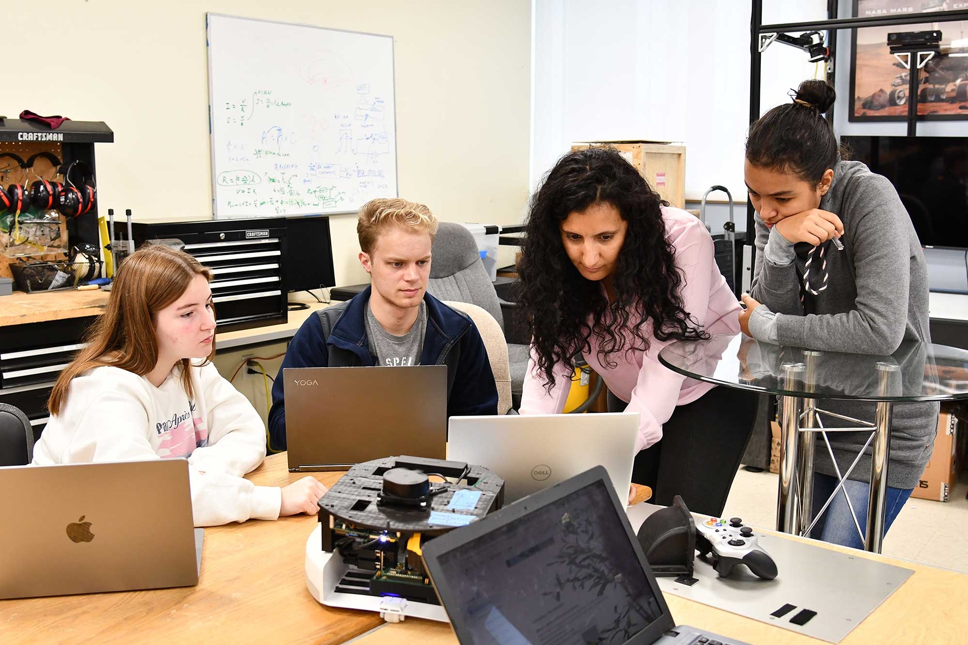 3 students and a professor lean in to look at a computer screen