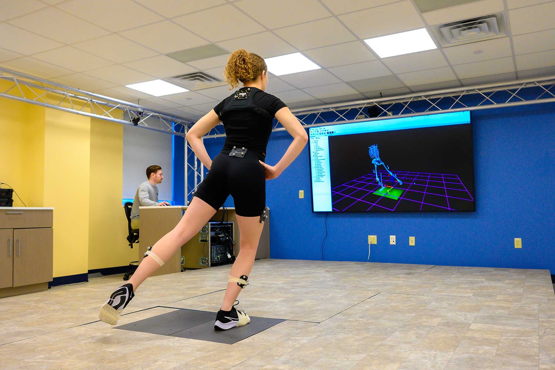A student wearing sensors moves as their motion is displayed on a large screen.