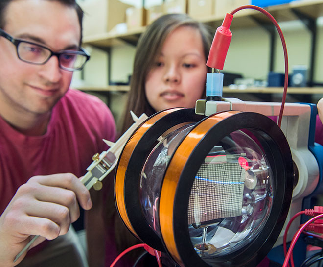 Two students work with a piece of equipment in a physics laboratory