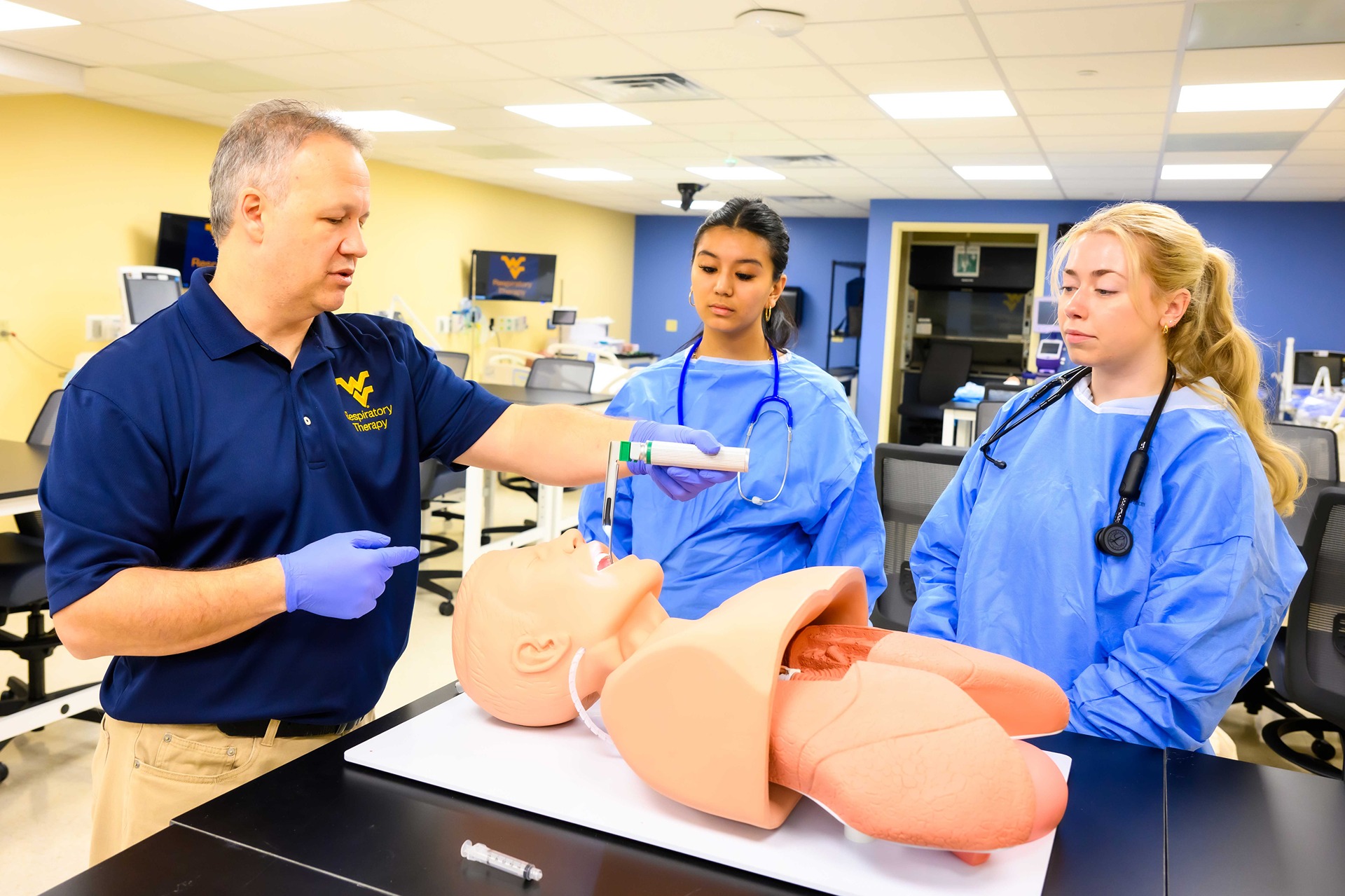 Instructor uses a patient simulator to demonstrate intubation as 2 students watch.