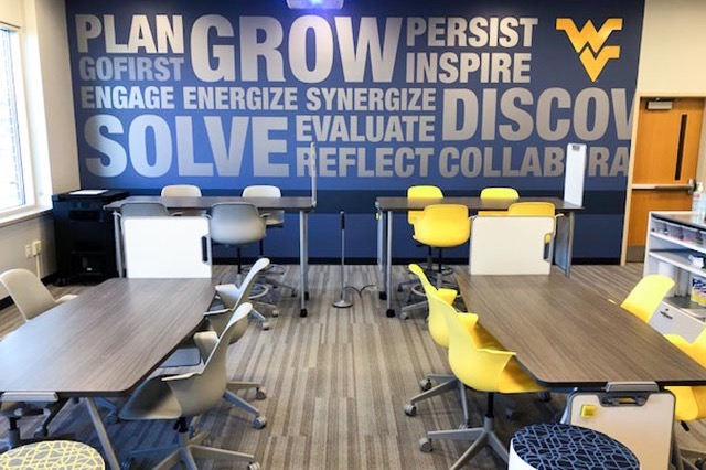 Modern meeting space with tables, chairs, and a gold and blue WVU mural