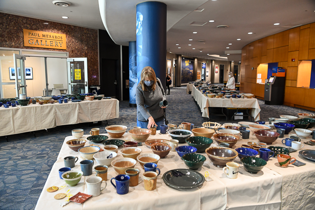 The CCAC Lobby Filled with student made pottery for sale as someone exploring options on a table of bowls and mugs.
