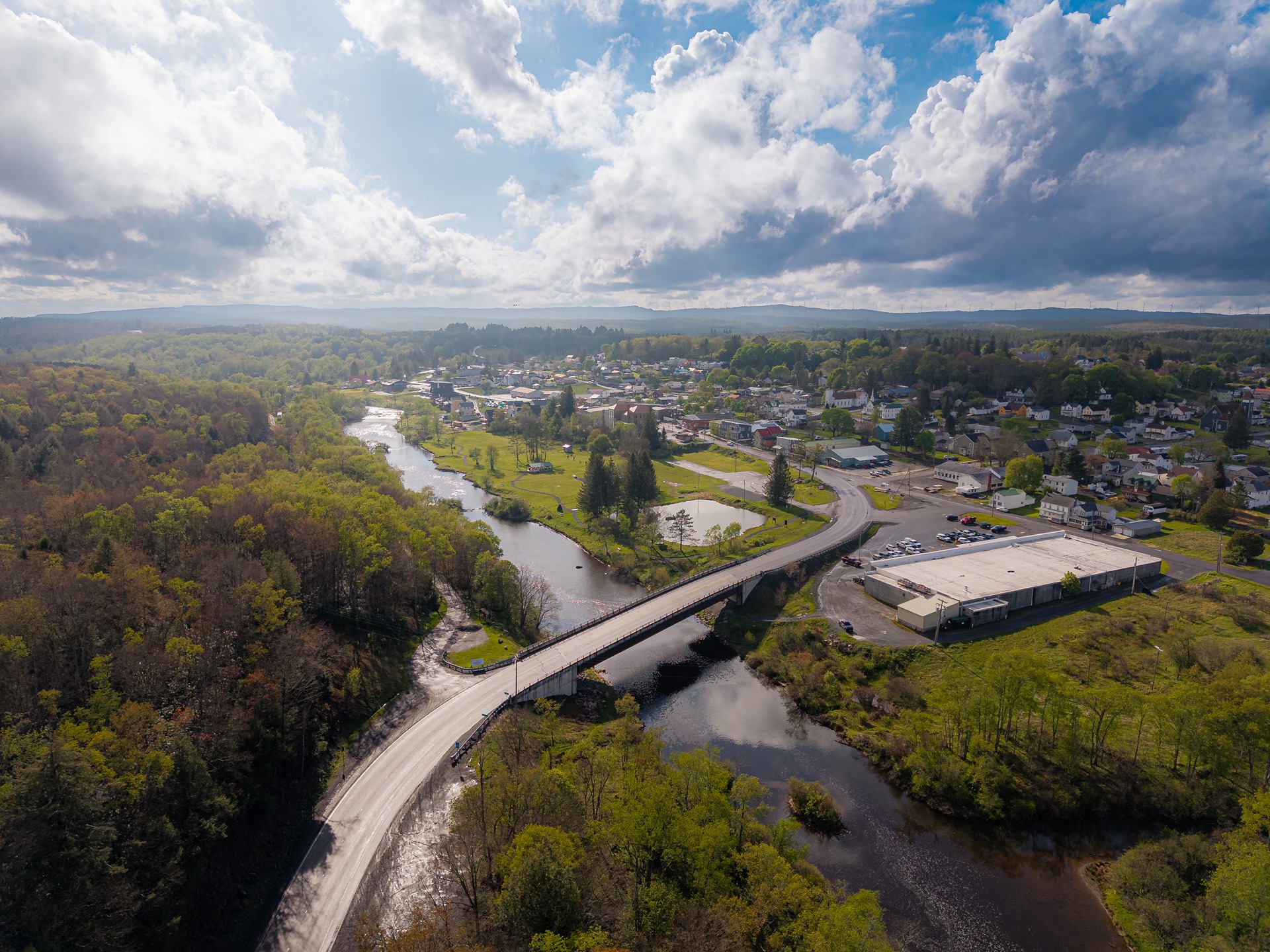 Aerial view of a West Virginia town, river and bridge surrounded by forested mountains.